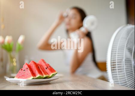 Immagine ravvicinata di un piatto con cocomeri su un tavolo con una donna surriscaldata sullo sfondo. estate calda, attacco di calore, alta temperatura, liv Foto Stock