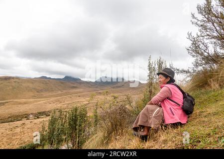 Una donna indigena solitaria seduta sulla cima di una collina si affaccia sul selvaggio e desolato alto paese delle Ande vicino a Quito, in Ecuador. Foto Stock