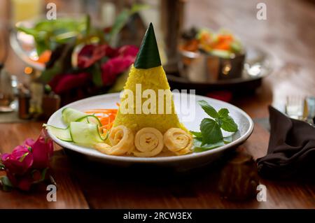 Nasi Tumpeng Mini. Riso giallo a forma di cono. Un piatto di riso indonesiano festoso con contorni. Foto Stock