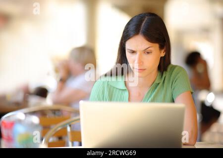Ritratto frontale di una donna sospetta che utilizza un computer portatile sulla terrazza di un ristorante Foto Stock