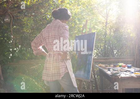 Donna birazziale che indossa grembiule che guarda la pittura su cavalletto in giardino Foto Stock