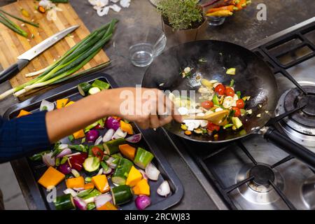 Sezione centrale della donna birazziale che indossa il grembiule che cucina la cena in cucina Foto Stock
