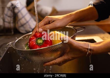 Parte centrale della donna birazziale che indossa grembiule lavando verdure in cucina Foto Stock