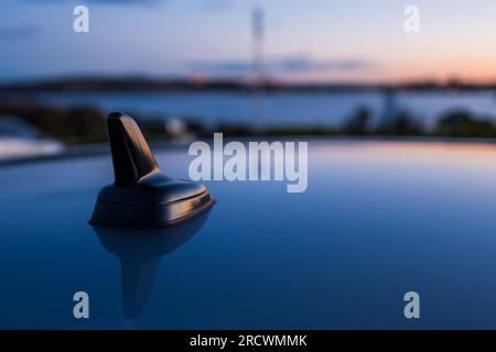 Primo piano dell'antenna nera per auto su un tetto contro il cielo luminoso del tramonto Foto Stock