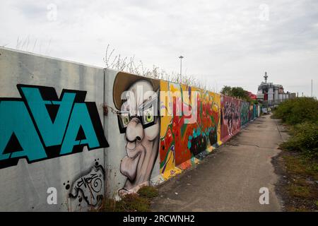 Opere d'arte sui graffiti sulle pareti del mare lungo il Tamigi, Thurrock, vicino a Grays, Essex. Procter and Gamble Factory a distanza. Foto Stock