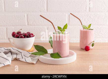 Due eleganti bicchieri con frullati di ciliegia appena fatti e una ciotola di ciliegie mature sul ripiano inferiore. Una bevanda deliziosa e salutare. Disintossicazione Foto Stock