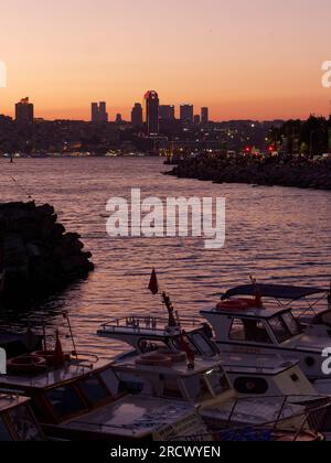 Le barche in primo piano e la gente siede sulle rocce e goditi un tramonto sul Mare del Bosforo da Uskudar Istanbul, Turchia. Zona occidentale della città dietro. Foto Stock