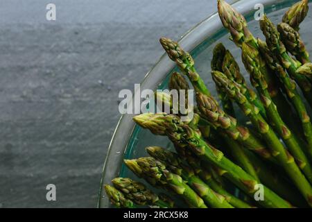 Primo piano delle punte degli asparagi nel recipiente sul piano di lavoro in ardesia Foto Stock