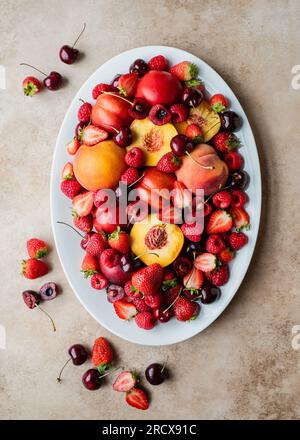 Vista dall'alto di un grande piatto di frutta mista: Frutti di bosco, pesche, ciliegie. Foto Stock