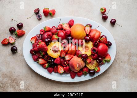 Vista dall'alto di un grande piatto di frutta mista: Frutti di bosco, pesche, ciliegie. Foto Stock