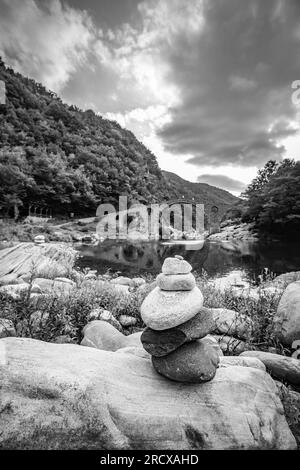 Piccola pila Zen di pietre, vista poco profonda di fronte al ponte del Diavolo sul fiume Arda, Bulgaria meridionale. Immagine di viaggio in bianco e nero Foto Stock