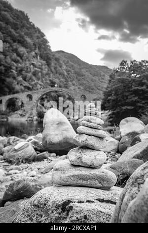 Piccola pila Zen di pietre, vista poco profonda di fronte al ponte del Diavolo sul fiume Arda, Bulgaria meridionale. Immagine di viaggio in bianco e nero Foto Stock