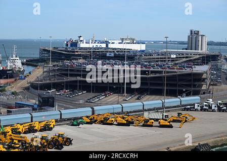 Un treno per il trasporto di auto e JCB gialli sul molo di Southampton, con auto in attesa di essere esportate. Foto Stock