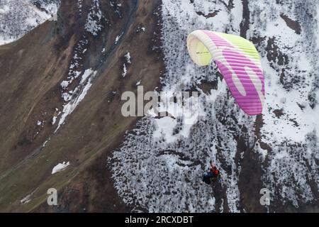 Gudauri, Georgia - 1° maggio 2019: Paesaggio montano con parapendio che vola di fronte alle cime innevate del Caucaso di giorno Foto Stock