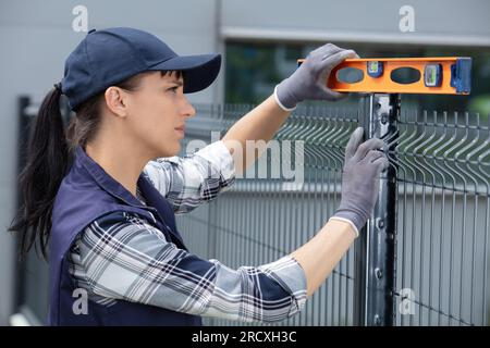 il lavoratore in uniforme blu controlla il livello di una recinzione Foto Stock