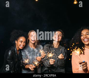 Quattro femmine felici con scintillanti. Gruppo di diverse amiche femminili che festeggiano di notte. Foto Stock