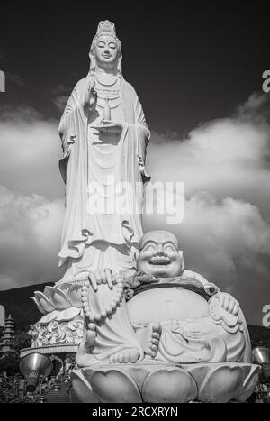 Una statua Budai, o Buddha ridendo, davanti alla statua gigante di Avalokitesvara Bodhisattva nella pagoda buddista Ling Ung Bai Buc in Son tra, Danang, Foto Stock