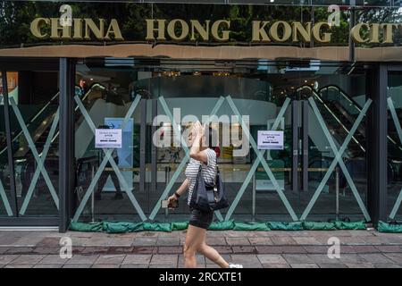 Una donna cammina davanti a un centro commerciale chiamato China Hong Kong City durante il segnale di avvertimento n. 8. Nelle prime ore del 17 luglio, quando il tifone Talim si avvicina a Hong Kong, l'Osservatorio di Hong Kong emette il segnale di allarme del tifone n. 8 alle 00:40 del mattino Questo segnale porta cambiamenti significativi in tutta la città, con la maggior parte dei servizi di autobus che si fermano e il mercato azionario chiude le porte in risposta al pericolo imminente. Tuttavia, in mezzo a queste misure precauzionali, la MTR (Mass Transit Railway) continua a fornire servizi di metropolitana limitati, garantendo che residenti e viaggiatori abbiano un mezzo di t Foto Stock