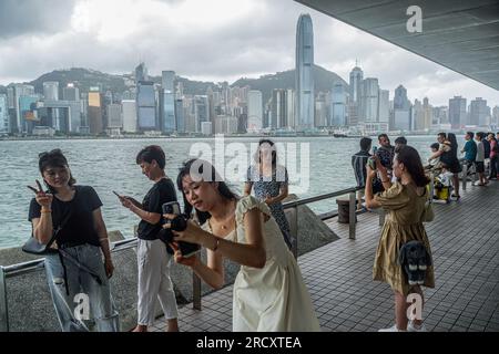 I viaggiatori scattano foto durante il segnale di avvertimento n. 8 a Tsim Sha Tsui. Nelle prime ore del 17 luglio, quando il tifone Talim si avvicina a Hong Kong, l'Osservatorio di Hong Kong emette il segnale di allarme del tifone n. 8 alle 00:40 del mattino Questo segnale porta cambiamenti significativi in tutta la città, con la maggior parte dei servizi di autobus che si fermano e il mercato azionario chiude le porte in risposta al pericolo imminente. Tuttavia, in mezzo a queste misure precauzionali, la MTR (Mass Transit Railway) continua a fornire servizi di metropolitana limitati, garantendo che residenti e viaggiatori abbiano un mezzo di trasporto durante questo periodo Foto Stock