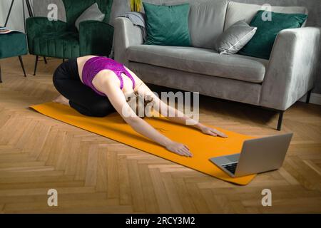 Donna in forma che pratica yoga in posa su un tappetino a bordo piscina con un tablet digitale davanti. Foto Stock