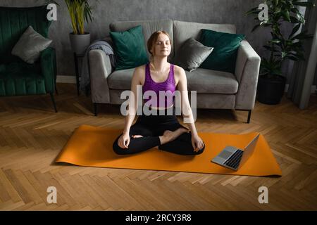 Donna in forma che pratica yoga sul tappetino utilizzando un programma di allenamento online sul suo tablet. Fitness, tecnologia e stile di vita sano Foto Stock