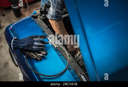 Meccanico caucasico che si prende cura di un motore per auto d'epoca. Esecuzione della manutenzione del veicolo. Foto Stock