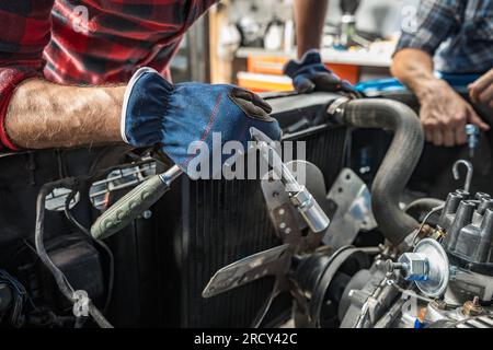 Meccanico caucasico professionista che si prende cura di un motore per auto d'epoca. Tema American Muscle Cars. Foto Stock