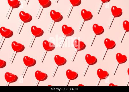 Motivo lollypop rosso a forma di cuore senza cuciture su sfondo rosa. Vista dall'alto. Rendering 3D. Foto Stock