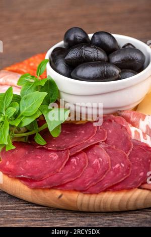 Primo piano di pastrami a fette, olive nere e basilico verde. Messa a fuoco selettiva. Foto Stock