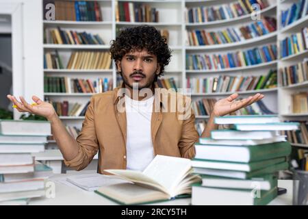 Studente insoddisfatto e frustrato che cerca di concentrarsi e prepararsi per l'esame da solo, uomo seduto in biblioteca stanco di studiare e imparare il materiale da solo. Foto Stock
