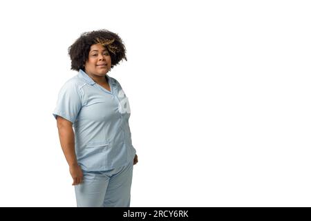 giovane infermiera afro-latina di etnia venezuelana, si trova in piedi in posa in uniforme blu sorridendo e guardando la telecamera su sfondo bianco e felice Foto Stock
