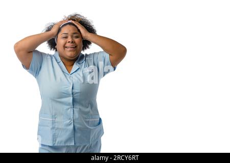 Giovane donna bruna afro-latina che indossa un cerchietto per la pulizia del viso e un'uniforme blu, sorridente sorprende guardando la fotocamera, sfondo bianco con c Foto Stock