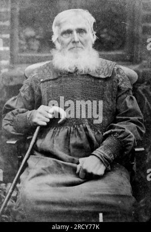 Ritratto seduto di un uomo anziano con i capelli bianchi e la barba, stringendo un bastone da passeggio di legno. Fotografia originale non attribuita. Da una collezione di fotografie vittoriane carte de visite, datate al 1890 Carte de visite è un termine francese conosciuto in inglese come "carta da visita". Di solito avevano una stampa fotografica in albume di circa 54x89 mm montata su una scheda leggermente più grande. In alcuni casi, le devastazioni del tempo hanno preso il loro tributo. Foto Stock