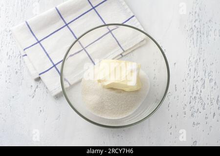 Recipiente di vetro con zucchero e un pezzo di burro su sfondo azzurro, vista dall'alto. Cucinare torte al latte fatte in casa, fai da te, passo dopo passo, passo 1. Foto Stock