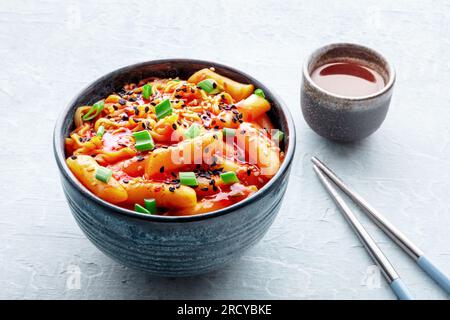 Rabokki, tteokbokki o topokki con ramen, Street food coreano, torte di riso speziate, bacchette e una bevanda Foto Stock