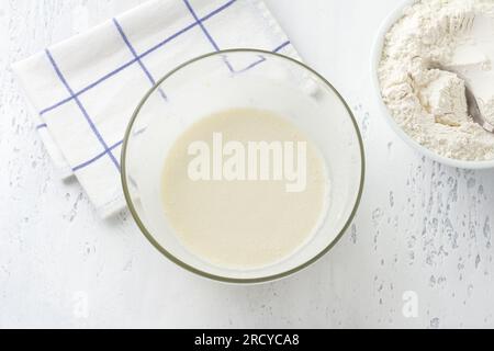Una ciotola di vetro con una massa montata di uova, burro, zucchero e latte su sfondo azzurro, vista dall'alto. Cucinare torte al latte fatte in casa, fai da te, st Foto Stock