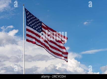 Stelle e strisce con bandiera USA di grandi dimensioni che soffiano nel vento con interessanti nuvole dietro nel cielo blu Foto Stock