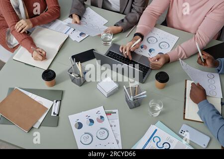 Sopra la vista del luogo di lavoro con documenti finanziari e mani di diversi giovani economisti interculturali che organizzano il lavoro durante le riunioni in ufficio Foto Stock