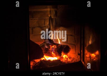 fuoco brucia con legna da ardere in un camino con riflesso in vetro su sfondo nero, festività di luci, natale, orizzontale Foto Stock