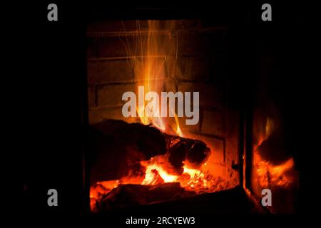 il fuoco brucia di legno in un camino con gas blu su sfondo nero, festività di luci, natale, orizzontale Foto Stock