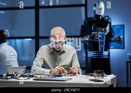 Ingegnere maturo che lavora con la scheda madre per lo sviluppo di robot in laboratorio Foto Stock