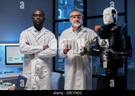 Ritratto di due ingegneri in camici bianchi che guardano la fotocamera mentre lavorano insieme in laboratorio Foto Stock