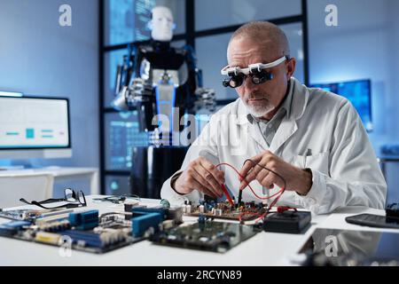 Ingegnere maturo in occhiali speciali che lavora con il sistema informatico al tavolo del laboratorio Foto Stock