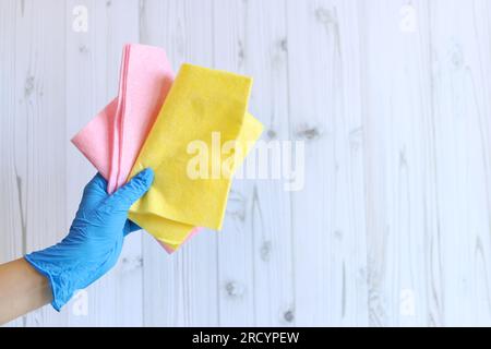 Panni per pulizia viscosa. La mano di una donna in un guanto di lattice blu contiene diverse salviette per la pulizia. Portare a mano uno straccio per la pulizia su uno sfondo di legno. Il co Foto Stock