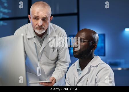 Due ingegneri multietnici che discutono di programmi informatici su computer mentre lavorano in team nel laboratorio Foto Stock