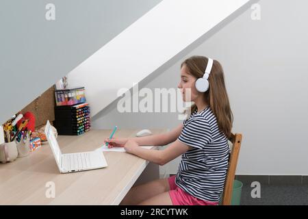 Un'adolescente scrive un'attività su un pezzo di carta di un computer. T-shirt a righe, camera luminosa Foto Stock