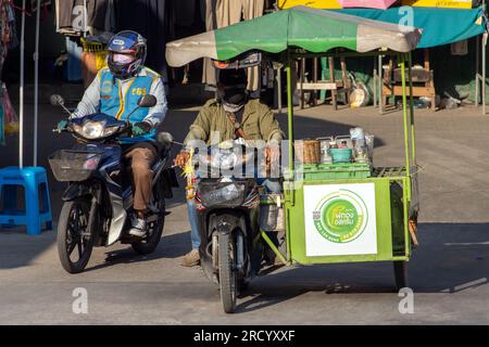 SAMUT PRAKAN, THAILANDIA, 07 2023 FEBBRAIO, un distributore di gelati cavalca una moto a tre ruote su una strada con stand Foto Stock