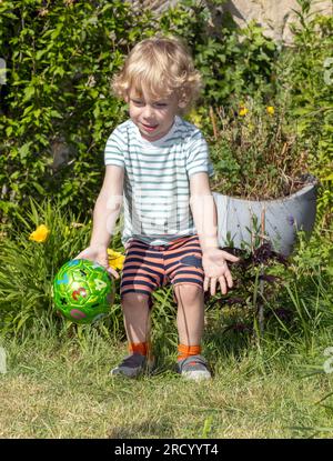 Un bambino prende una palla nel giardino estivo Foto Stock