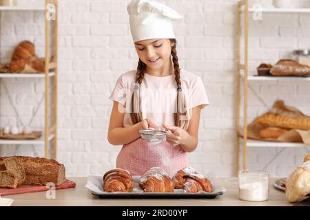 Piccolo panettiere cospargere lo zucchero in polvere sui croissant in cucina Foto Stock