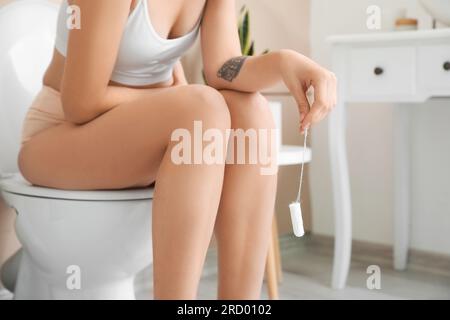 Giovane donna con un tampone seduta sulla ciotola del bagno, primo piano Foto Stock